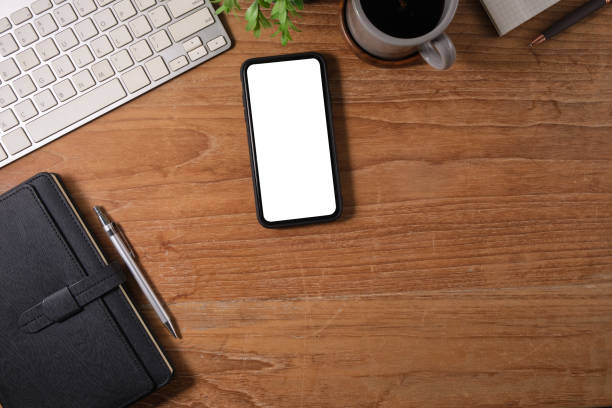 istock Top view of mobile phone with white screen, coffee cup and notepad on wooden table. 1500745831