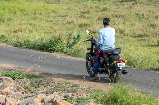 Pune, India - June 18 2023: Young Indian man on a motorcycle on a rural road at Uruli near Pune India.