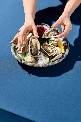 Vertical side view of a woman's hand picking up a fresh oyster, a luxury dining moment captured