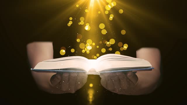 Magic Book on Magician Hand I Dark Background with Glowing Light Rays. The Fairy Tales and Magical Knowledge Concept