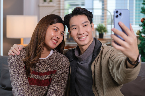 Happy y couple having fun making selfie on smart phone for social network while sitting on couch.