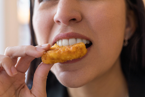 taking a bite of a piece of fried nugget, enjoying fast food, close up of the mouth, lips and teeth, lifestyle and tasting
