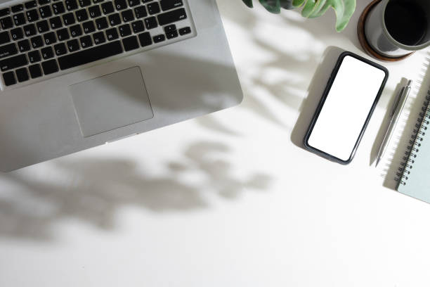 istock Top view of smart phone with empty screen, coffee cup, notepad and laptop on white table. 1500756188
