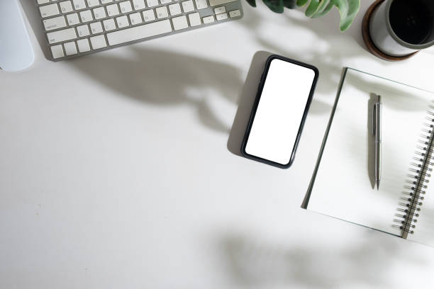 istock Top view of mobile phone with blank screen, notepad, coffee cup and keyboard on white table. 1500758005