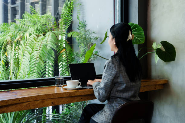 istock Beautiful Asian girl while working with laptop computer in bakery, typing. and there is a phone call coming in with a smartphone There are documents and coffee mugs on the table. sitting by the window 1500760281