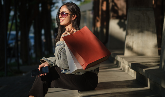 Side view of elegant fashionable woman in sunglasses carrying  shopping sitting on urban city staircase.