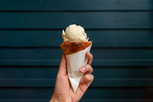 Scoop of sweet ice cream on croissant cone with wooden dark green wall background