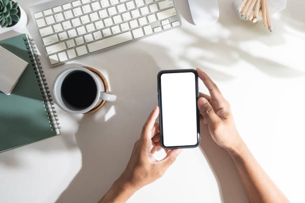 istock Above view of man hand holding smart phone with empty screen over white office desk. 1500762459