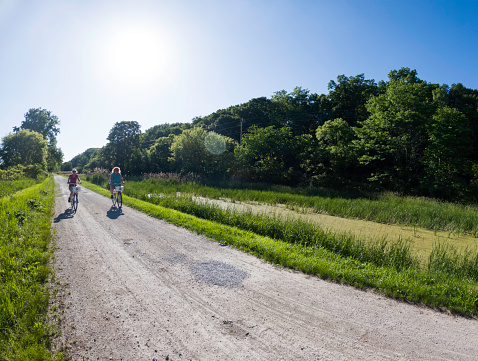 Two adult females ride bikes on a rural road in the country, Illinois, USA