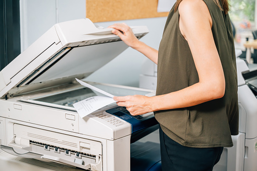 Confident secretary using modern printer and working at company, Female employee using copy print machine at office, Businesswoman placing document on scanner for copying