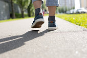 The child walks forward along the asphalt pavement in the rays of the sun in summer. View from the bottom of the legs of a child in sneakers walking along an asphalt road.
