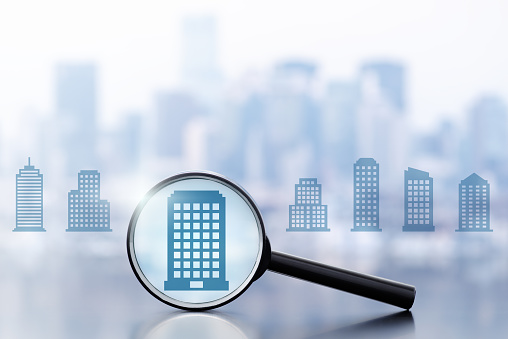 Magnifier and many building icons on cityscape background.