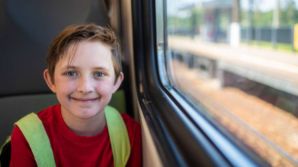 ragazzo sorridente di 10 anni che si siede vicino alla finestra nel treno elettrico dei pendolari in estate - 10 11 years cheerful happiness fun foto e immagini stock