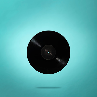 Antique blank LP vinyl record in mid-air on light blue background.