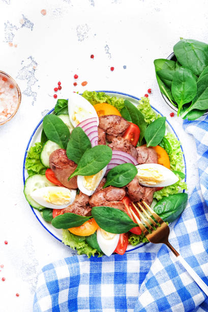 istock Perigord salad with roasted chicken liver, red tomatoes, cucumbers, boiled eggs, lettuce and spinach. Black kitchen table background, top view 1500787390