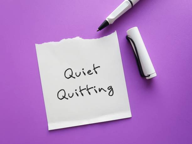 istock On purple background, pen writing on paper note QUIET QUITTING, when employees not engaged or taking job seriously, do minimum required but focus on job outside office 1500788272
