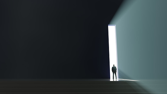 A man stood at a doorway looking towards the light.