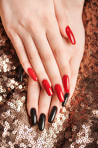 Hands of young girl with red  and black manicure on nails on sequins  background
