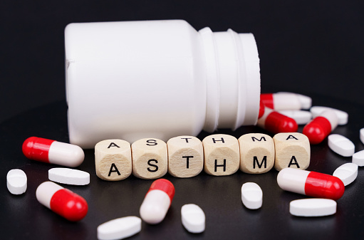 Medical concept. On a black background are red-white capsules, tablets, a jar and cubes with the inscription - ASTHMA