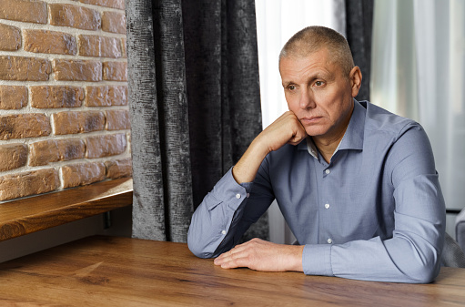 Portrait of a pensive middle-aged man sitting at a table. The man leaned his head on his hand looking to the side.