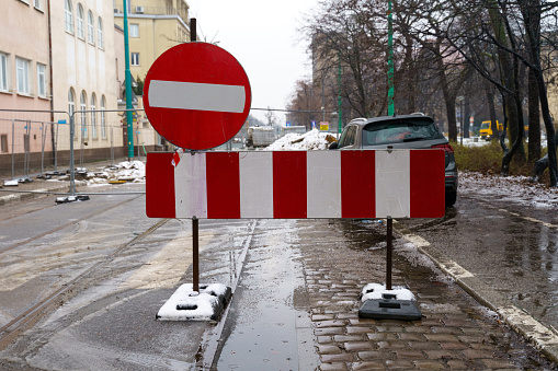 Road sign entry is prohibited, installed on a city street in front of a repaired section of the road. There is a car behind the sign.