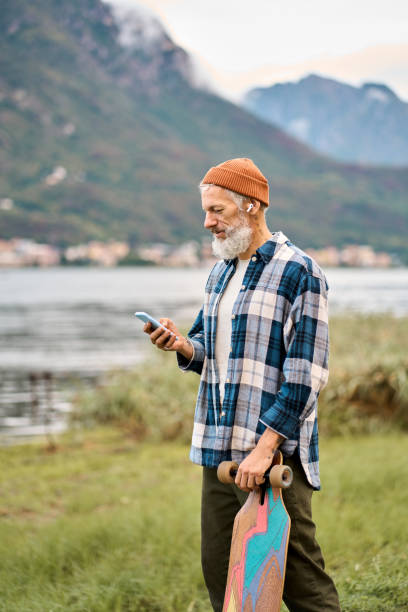 istock Active old hipster man standing in nature park holding skateboard using phone. 1500793824