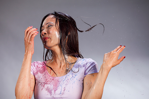 Asian woman being splashed with colored water. Red and blue. Surprise.