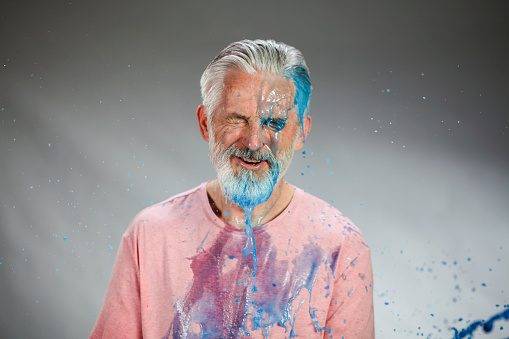 Mature man being splashed with colored water. Red and blue.