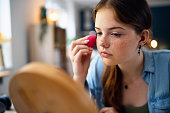 Teenage girl doing make-up in front of the mirror at her home