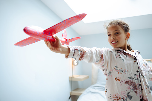 Little girl playing with airplane toy in bedroom in the morning