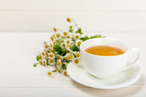 Chamomile tea in  cup on a white texture background. Natural hour with chamomile flowers. Herbal tea. Immunity tea.Natural healer concept. Healthy detox drink.Close up. Place for text.