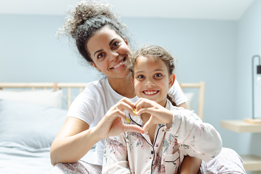 Portrait of mother and daughter in bed showing heart symbol