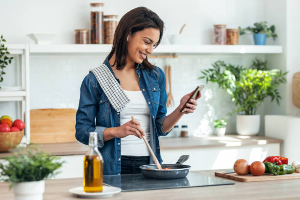 istock Beautiful smiling woman cooking while using mobile phone in the kitchen at home 1500809707