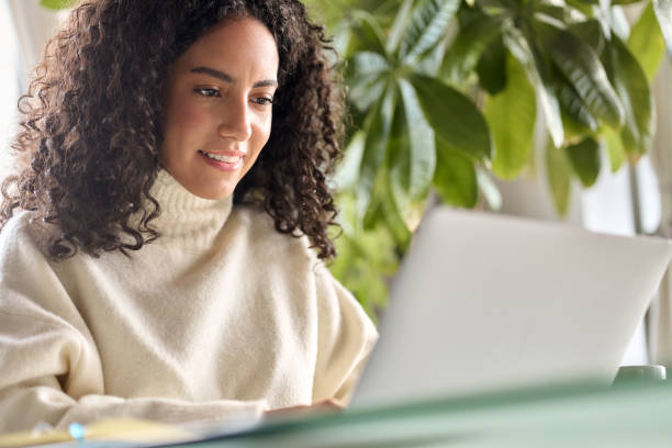 Young happy latin girl student using laptop looking at computer at home office.