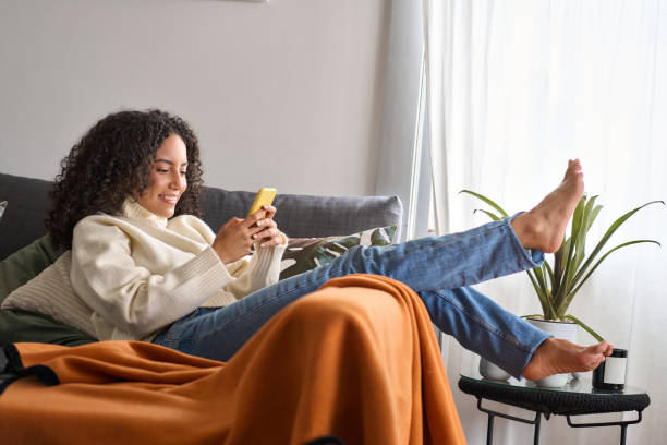 istock Smiling relaxed young latin woman sitting on couch using cell phone at home. 1500809829
