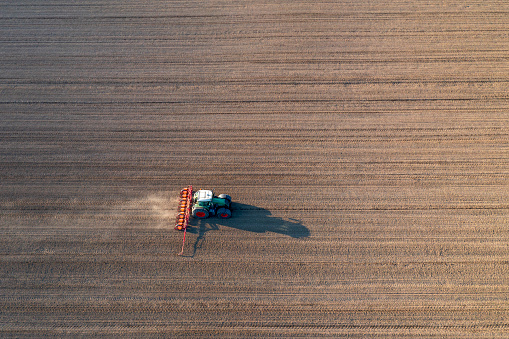 Tractor drilling seed in plowed field in spring viewed from above.