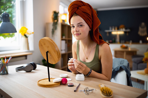 Portrait of Caucasian teenage girl, with hair wrapped in a towel, doing a beauty treatment at home.