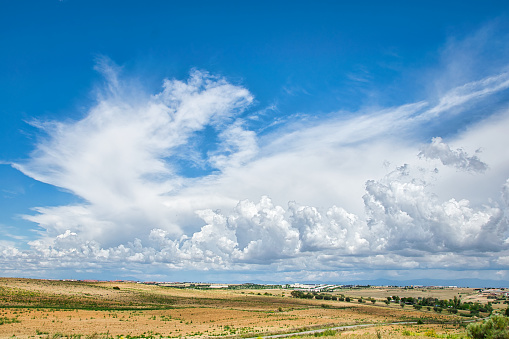 Large formations of cirrus and cumulonimbus clouds over a large expanse of cultivated fields.