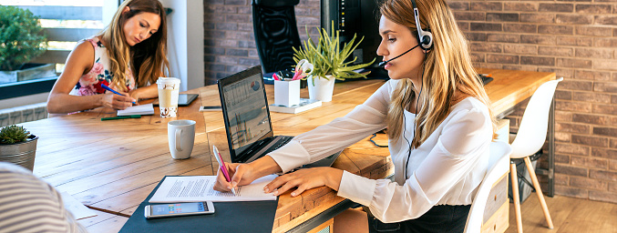 Young blonde woman with headset in customer help service of coworking. Assistance and support help concept.