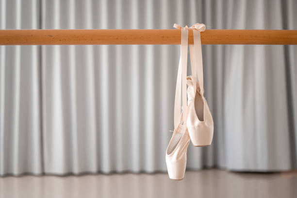 Pair of pink ballet shoes hanging on a wooden barre A pair of pink satin ballet pointe shoes with  satin ribbon hanging on a wooden barre in a ballet studio. ballet shoe stock pictures, royalty-free photos & images