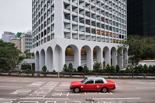 Hong Kong, China - April 24 2023: The Murray Hotel, with a red Taxi Passing in the Foreground