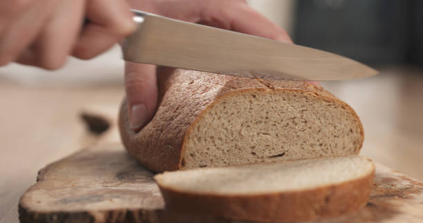 まな板の上でライ麦小麦の素朴なパンを�スライスする若い女性の手 - brown bread bread cutting board full length ストックフォトと画像