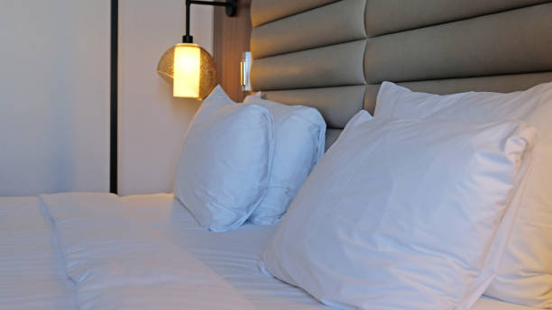 istock Close-up fragment of bedroom with empty bedside table, turn on reading lamp and a socket in modern interior​ design home or hotel. Soft pillow and blanket, stylish comfortable furniture. 1500814346