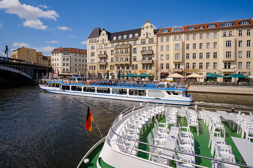 Berlin, Germany - April 18, 2023 : View of a touristic excursion boat at the river Spree, a bridge and various residential buildings in the background