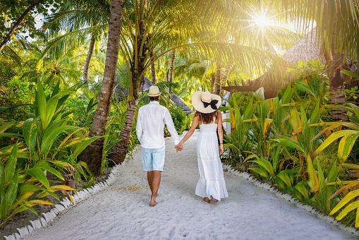 A luxury couple in white summer clothing walks on a tropical island with lush green and Palm Trees, Indian Ocean