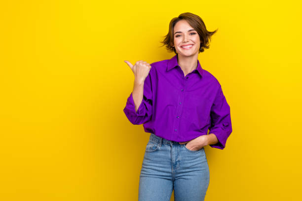 Portrait of attractive lady banker direct finger empty space wear violet blouse jeans pants isolated yellow vivid color background stock photo