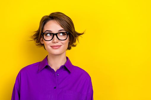 Photo portrait of attractive lady wondering look empty space wear eyeglasses violet blouse isolated yellow color background.