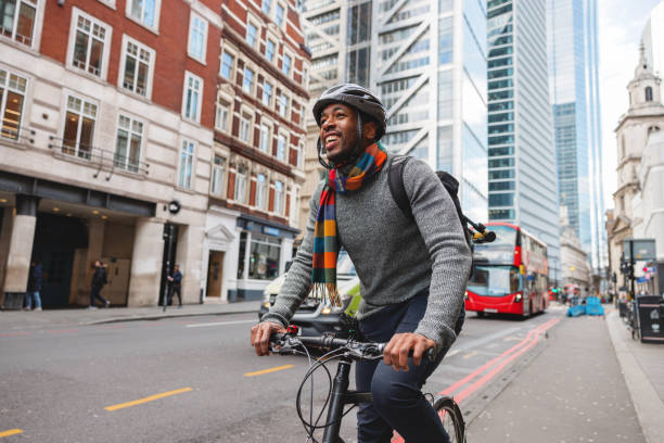 dorosły czarny świadomy ekologicznie mężczyzna uśmiechający się podczas jazdy na rowerze po mieście po pracy - bicycle london england cycling safety zdjęcia i obrazy z banku zdjęć