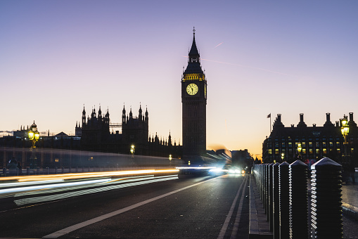 Long exposure photo of Westminster Palace and Big Ben from Westminster bridge in the evening. The sun has set and the sky is getting darker. The traffic lights are blurred.