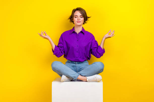 pełnowymiarowy portret spokojnej, ładnej dziewczyny siedzi na podium, sześcian, zamknięte oczy, medytujące, izolowane na żółtym tle; - yoga young adult cheerful happiness zdjęcia i obrazy z banku zdjęć